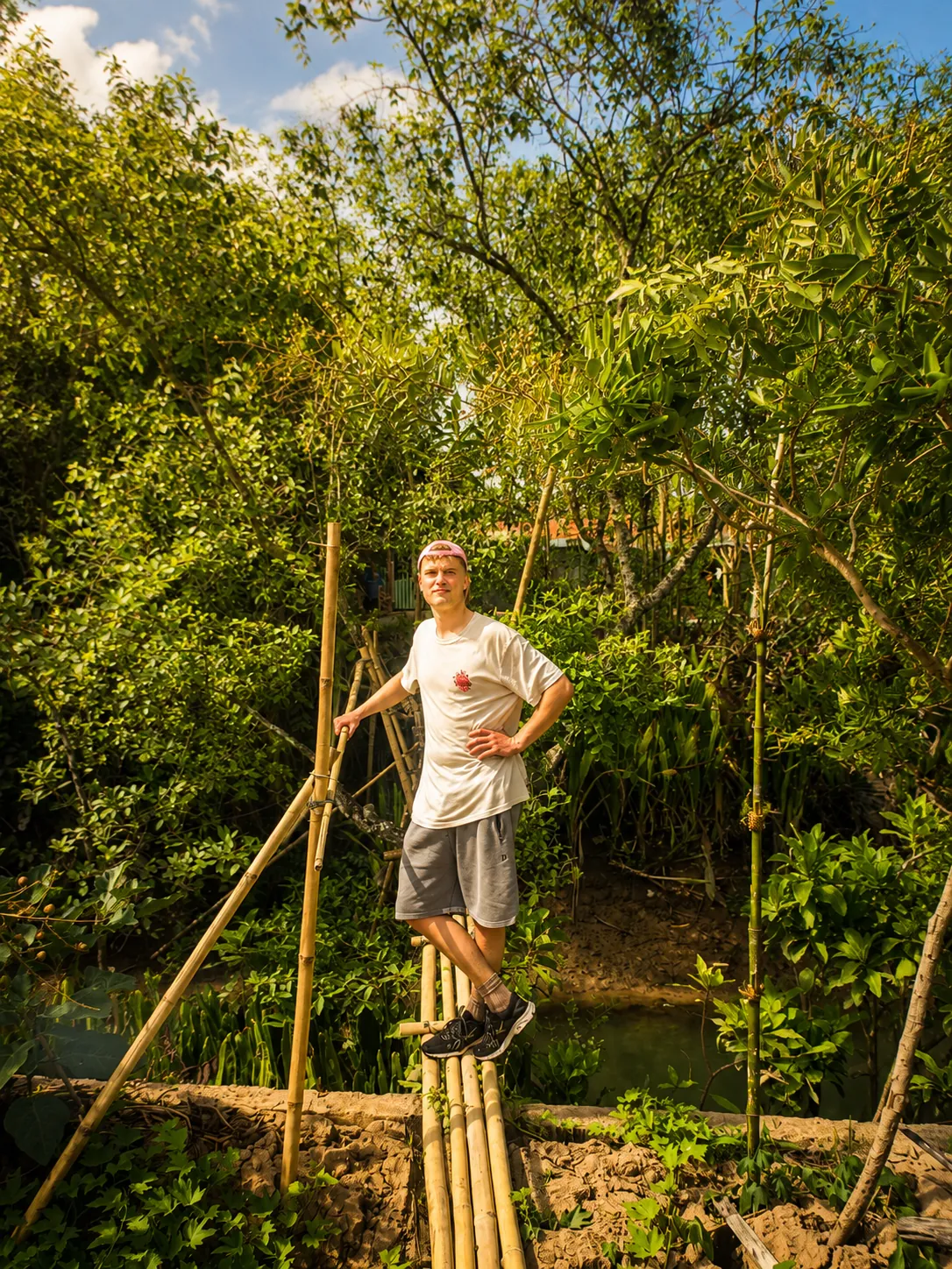 Visitor crossing a bamboo bridge surrounded by lush tropical greenery in Vinh Long