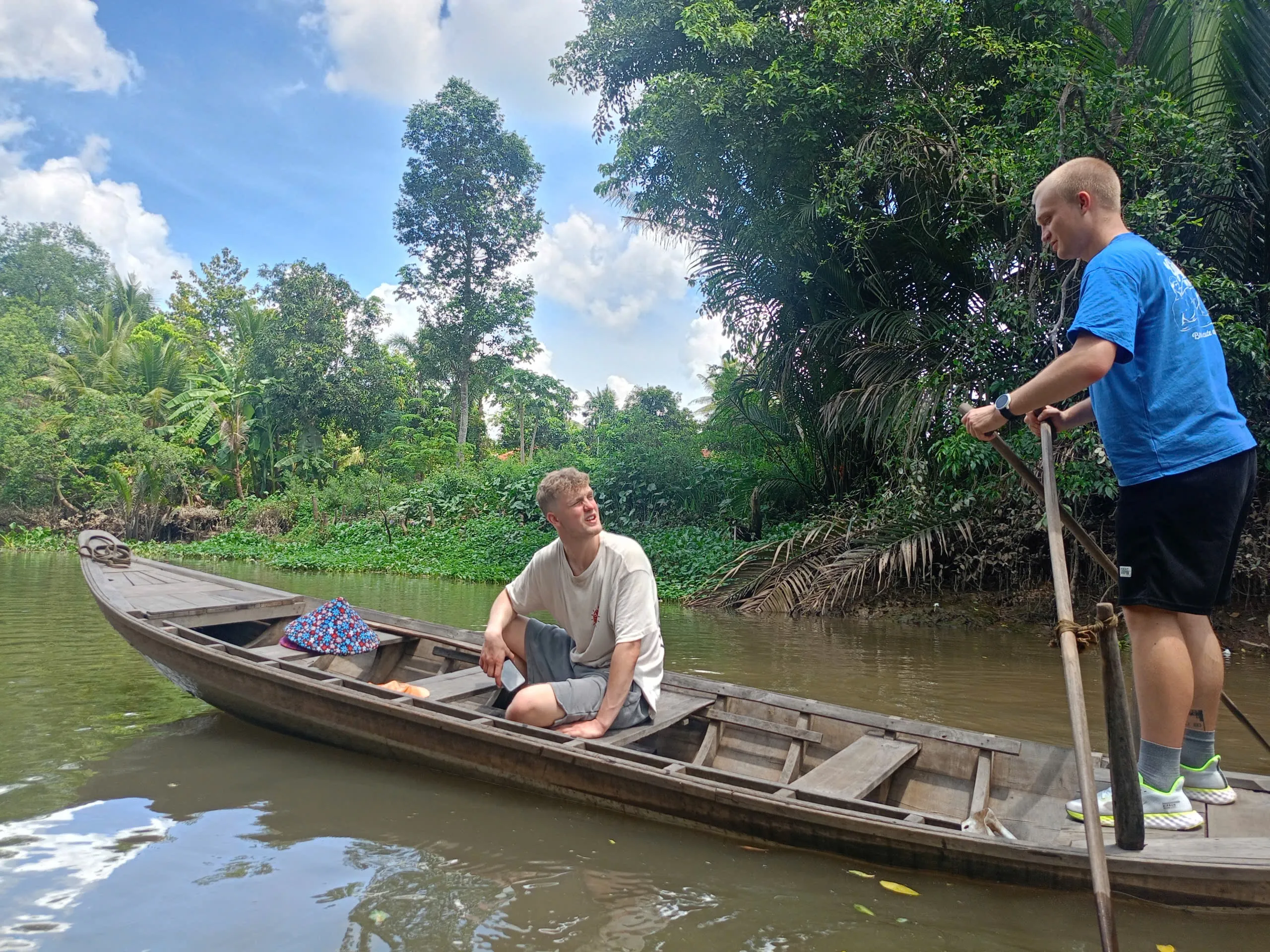 Two visitors rowing a wooden boat on a quiet Mekong Delta canal