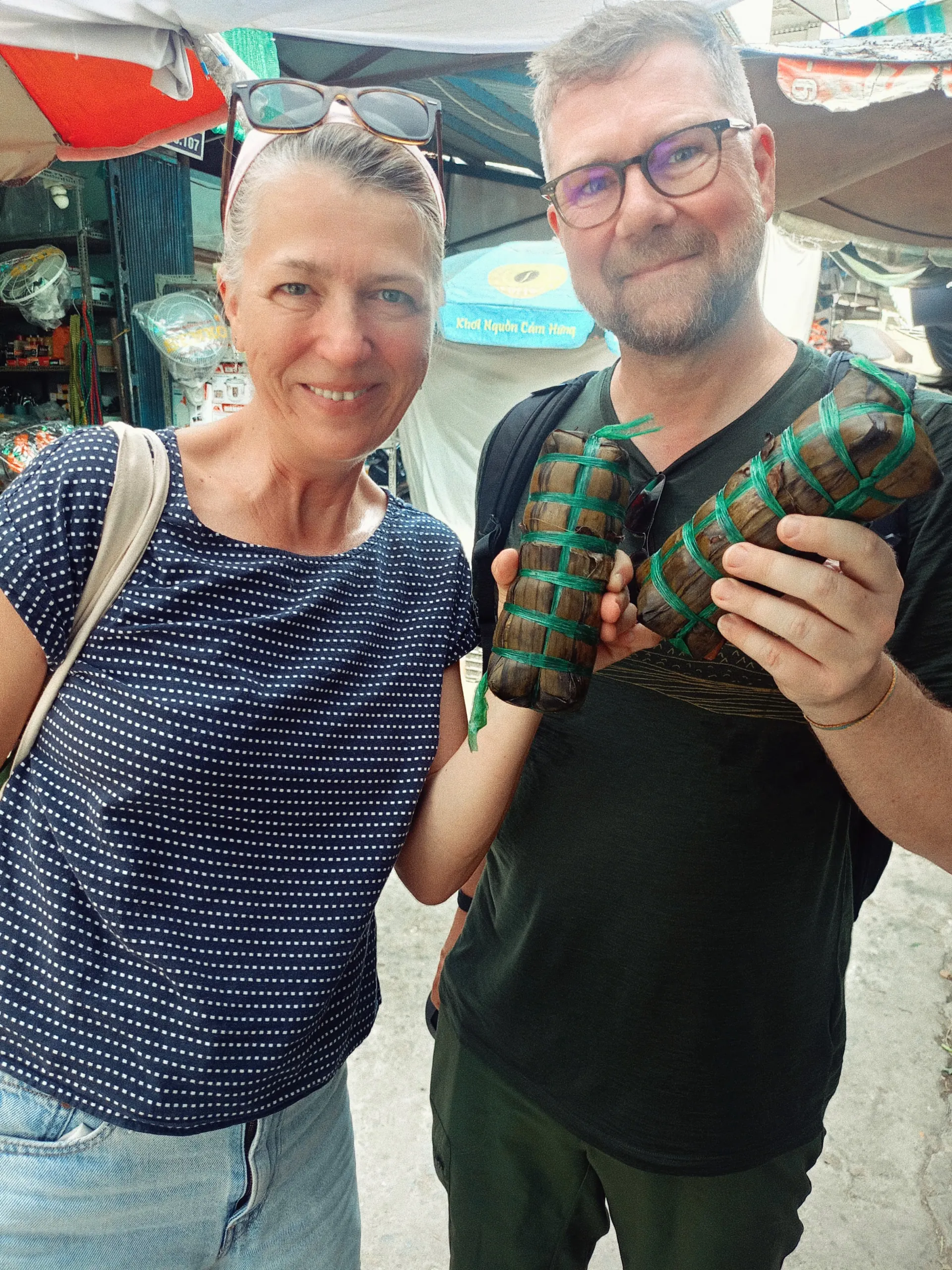 Travelers holding traditional bánh tét at a local market in Vinh Long
