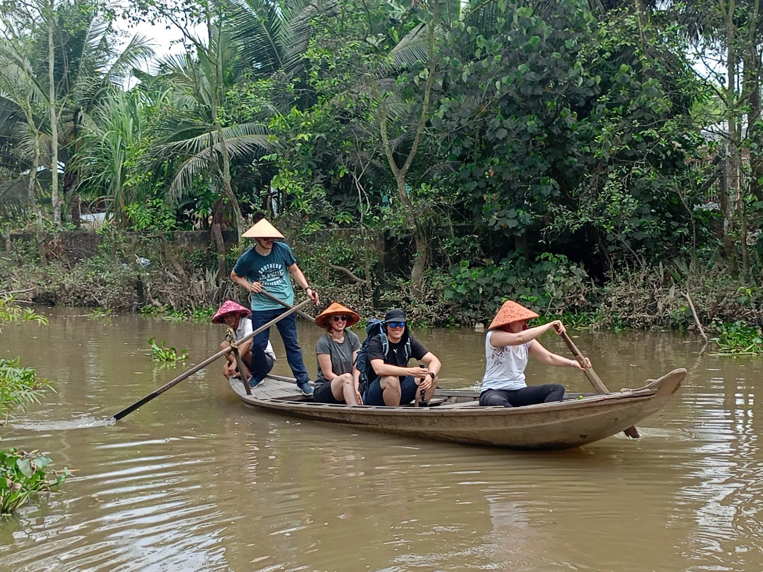 Visitors on a traditional rowing boat gliding through a small canal in Vinh Long