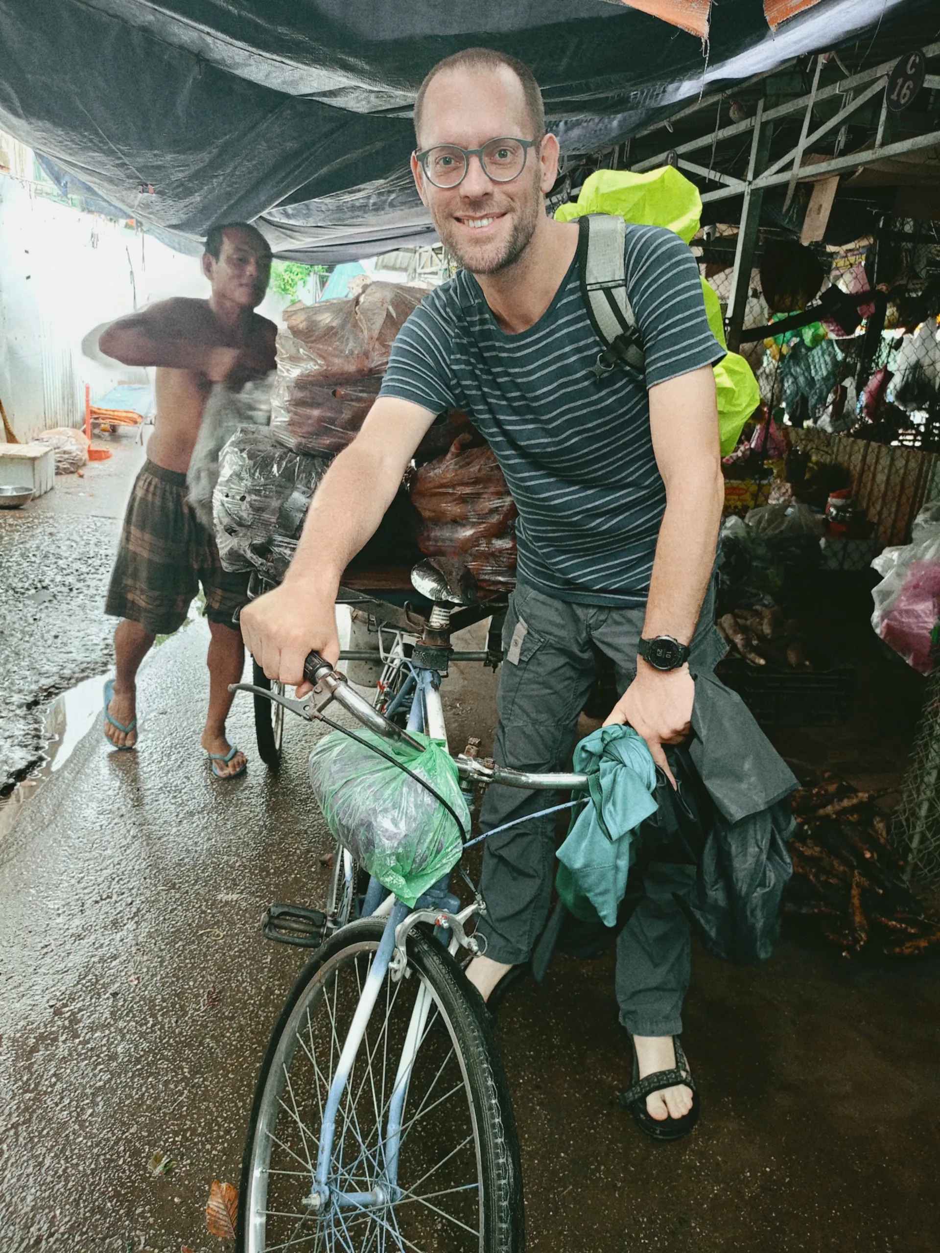 Cyclist smiling in the rain at a Vinh Long market — authentic Mekong Delta adventure