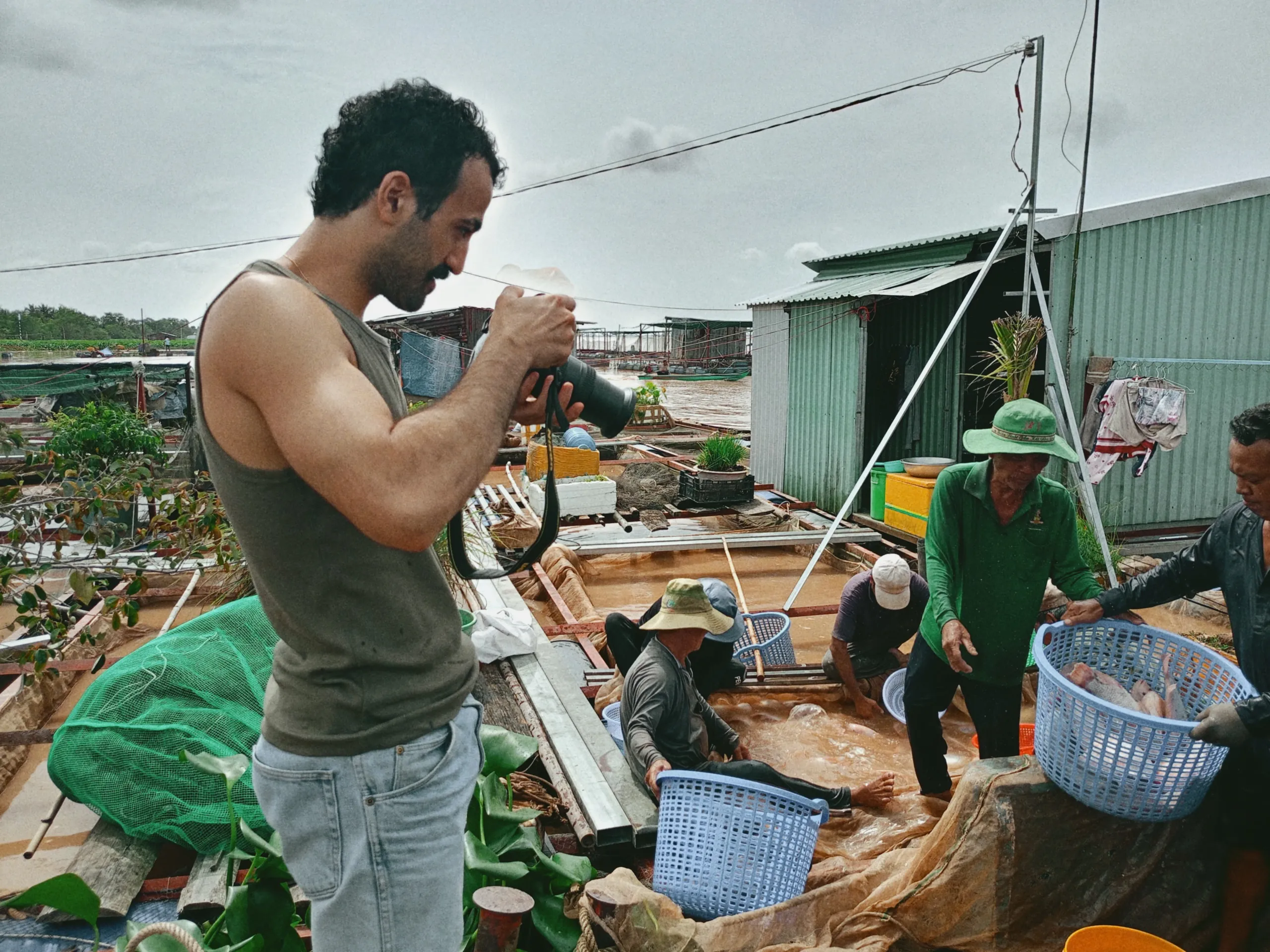 Visitor photographing local fishermen at a floating fish farm on the Mekong River